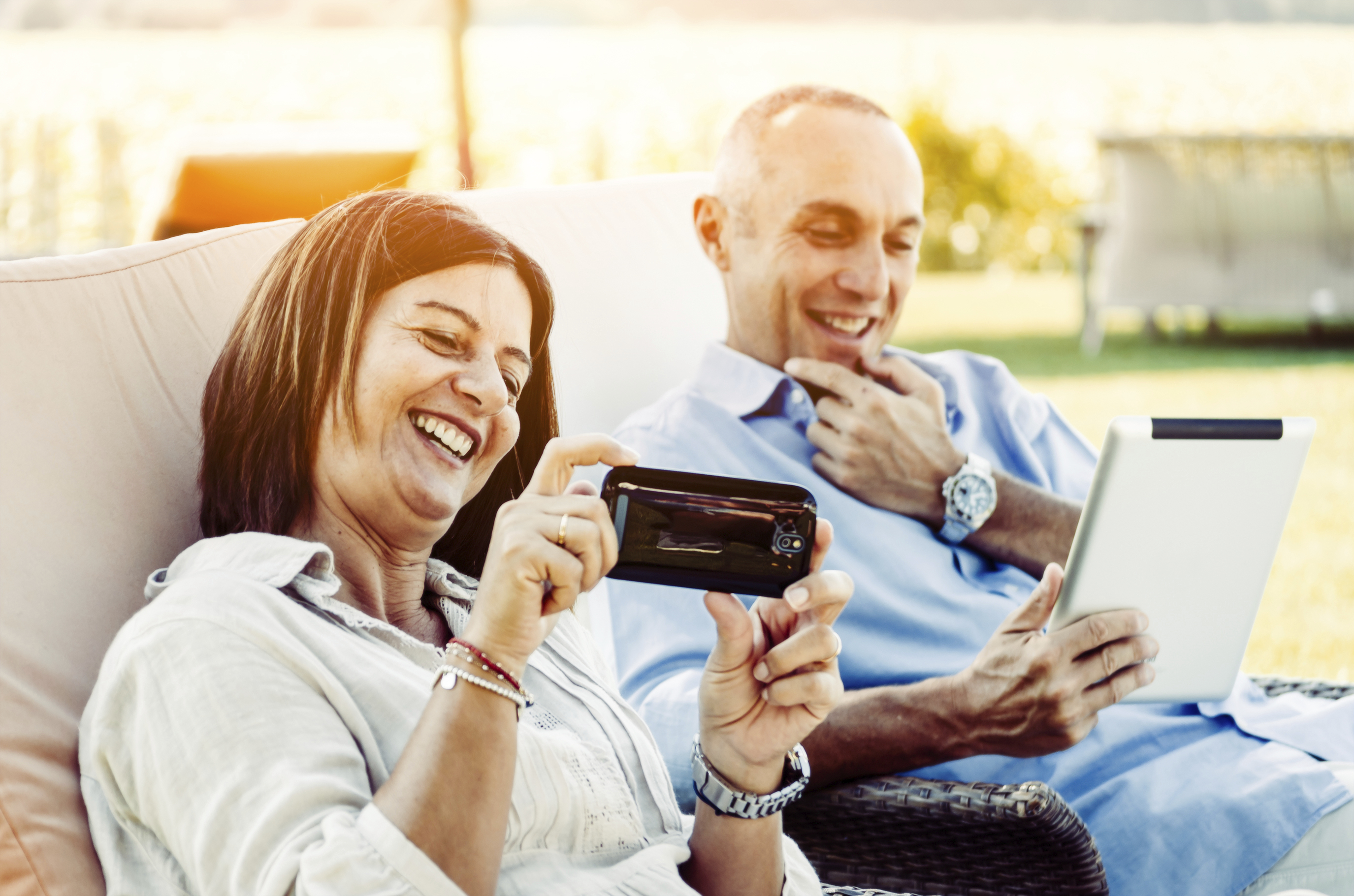 Husband and wife looking at Iphone and I Pad while smiling and laughing