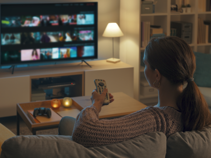 a woman watching tv and holding the tv remote pointed at the tv